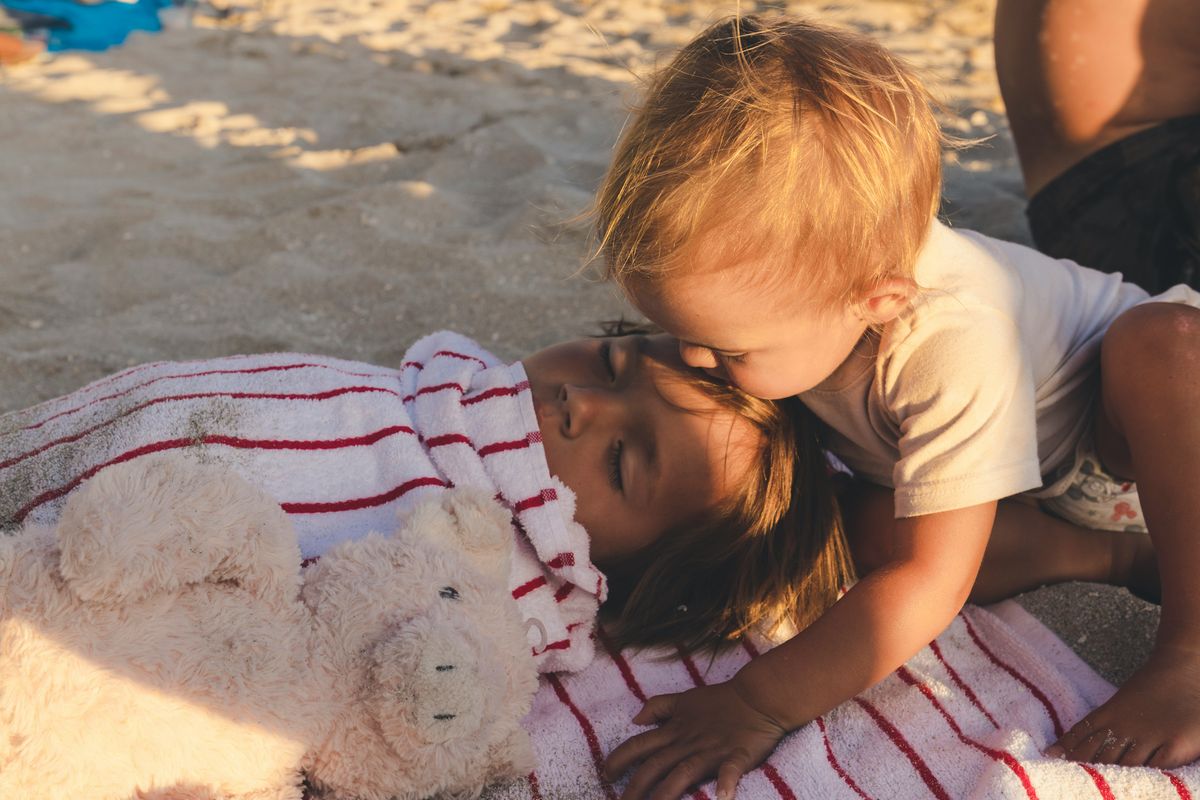Two young children resting together on the beach on holiday